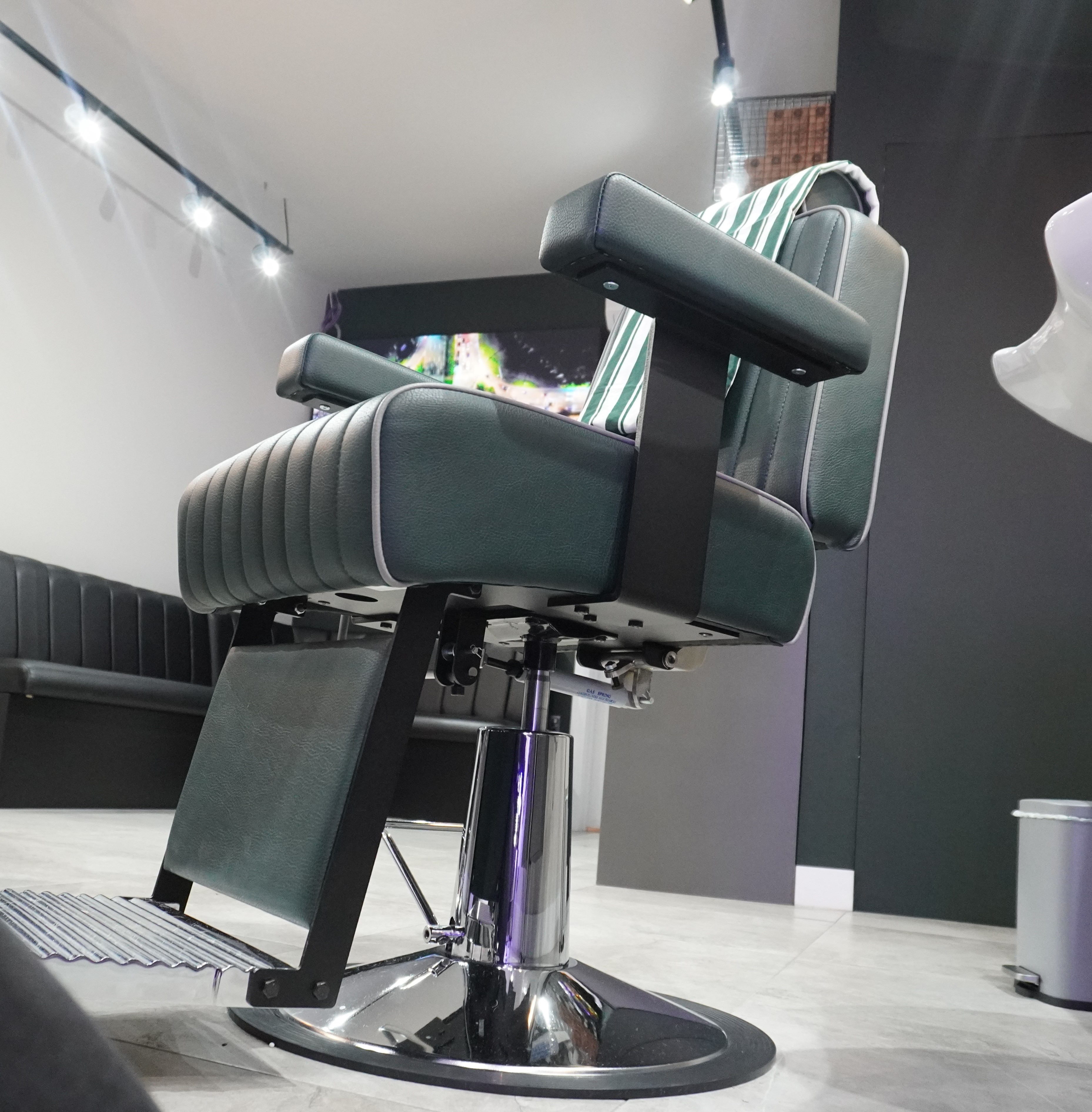 Modern barber chair in a barber shop interior with lit ceiling lights.